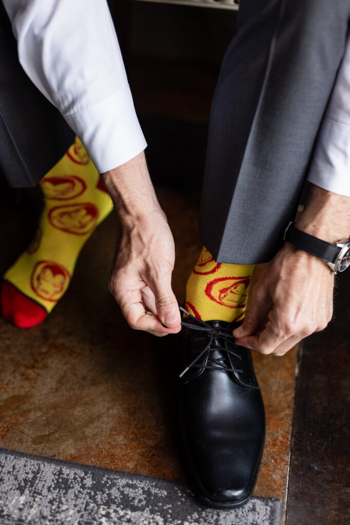 Groom tying black wedding shoes with Iron Man yellow and red socks