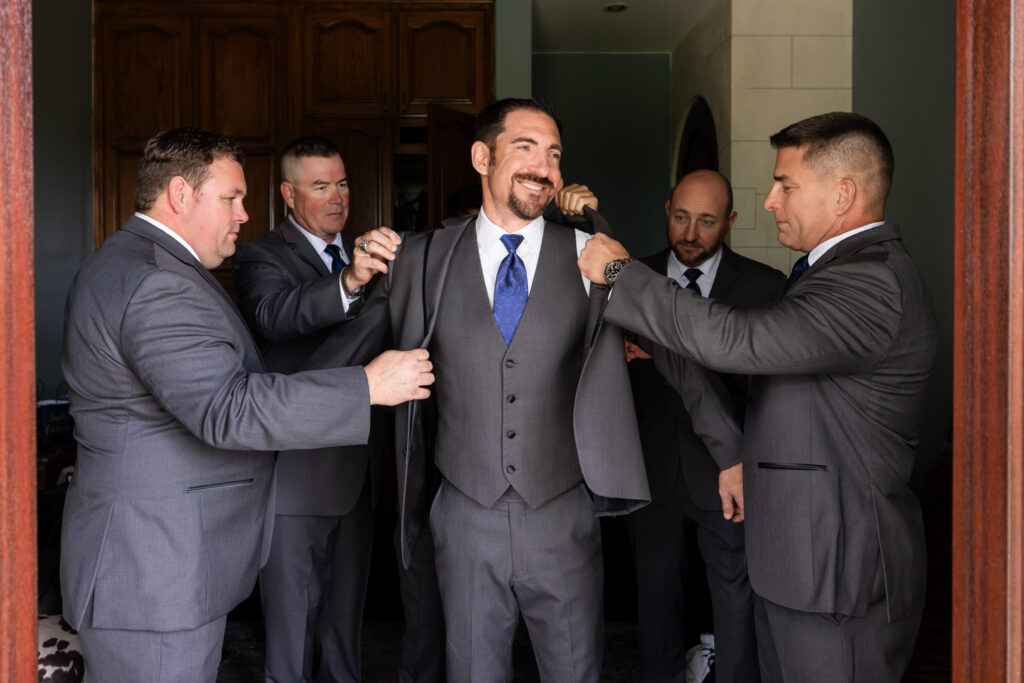 Groomsmen helping groom get into suit jacket