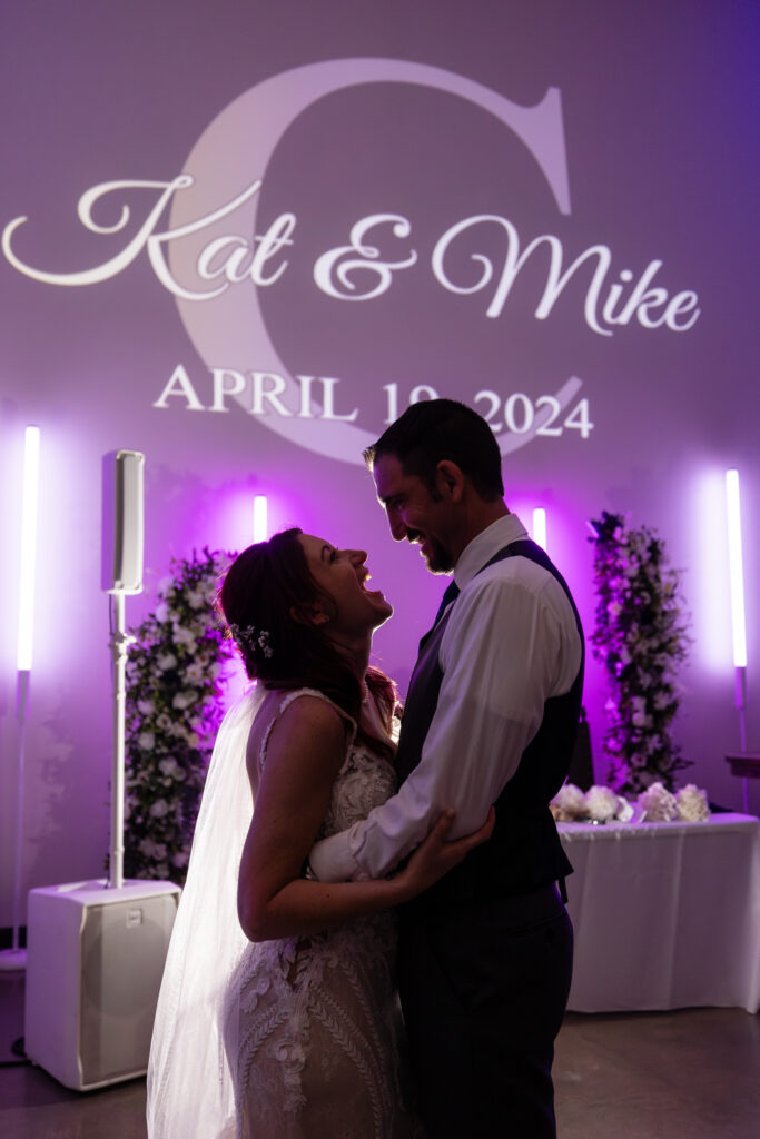 Bride and groom silhouette laughing on the dance floor with their custom monogram on the wall