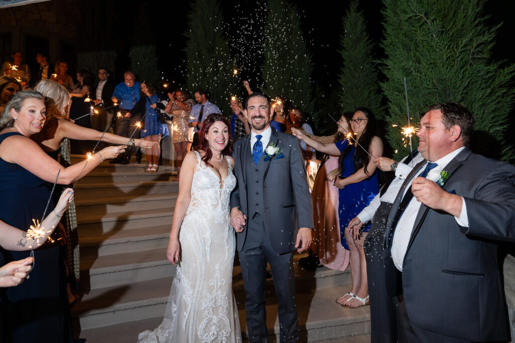 Bride and groom smiling and walking down staircase during sparkler exit with rice falling around them