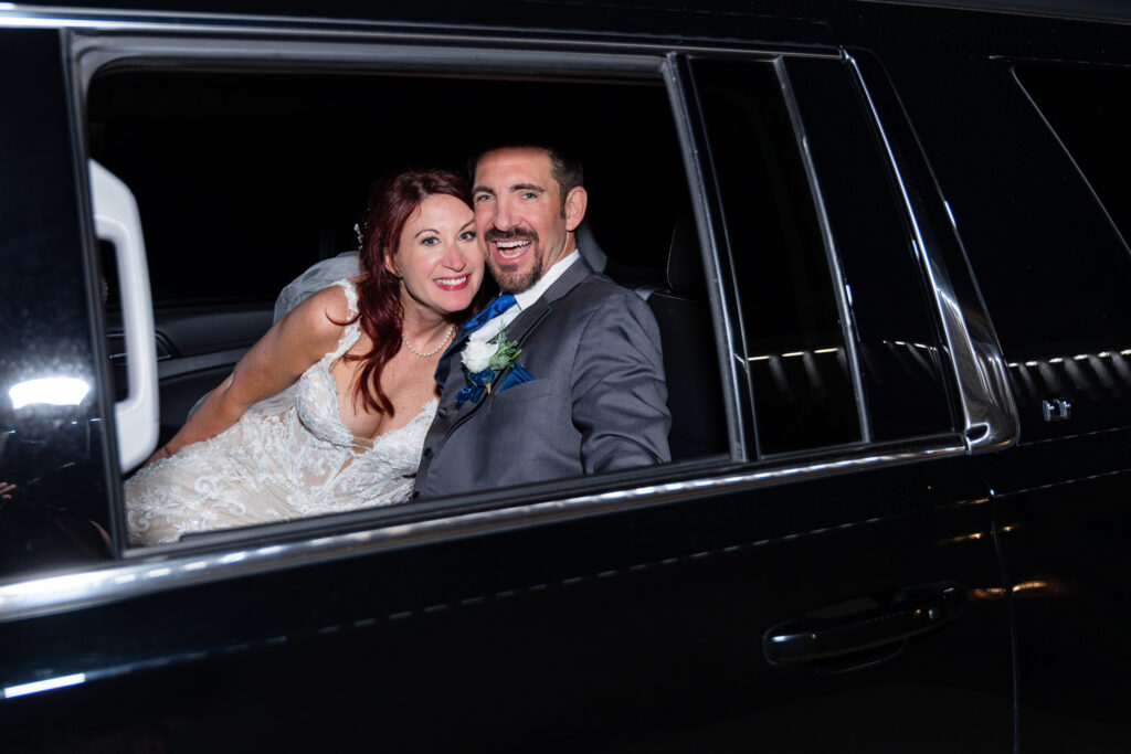 Bride and groom smiling in back of limo after wedding reception