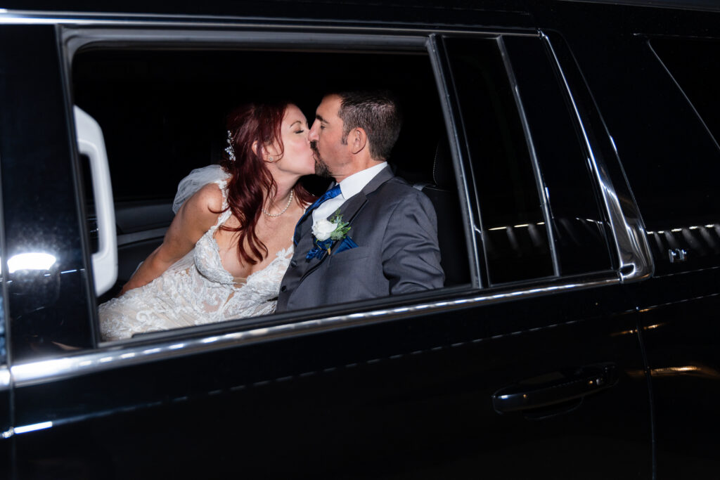 Bride and groom kissing in back of limo after wedding reception