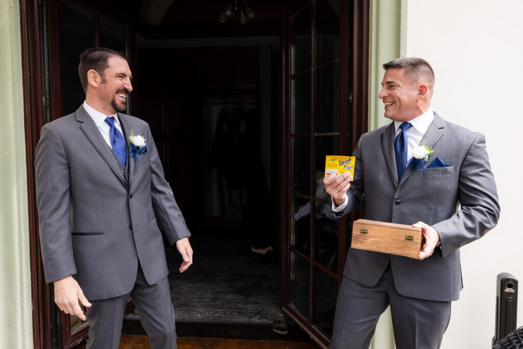 Groom gifting groomsmen a box of crayons and them both laughing