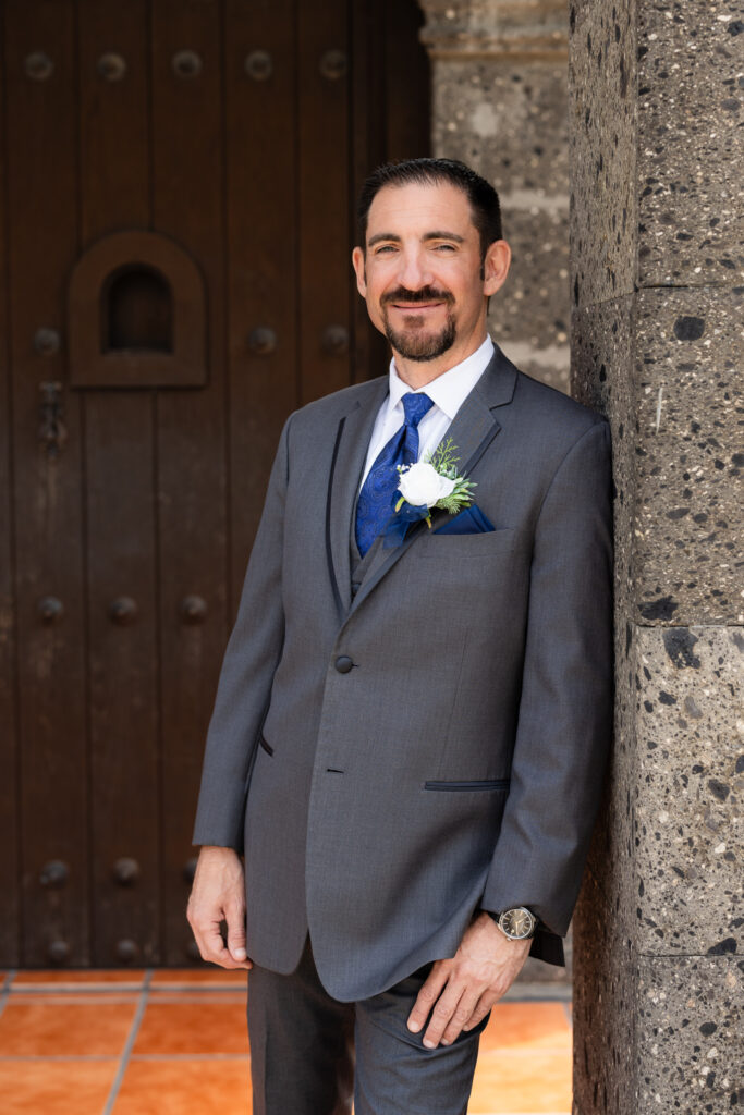 Groom leaning against column in front of Azle TX wedding villa smiling