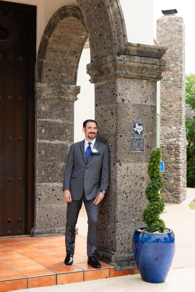 Groom leaning against column in front of Azle TX wedding villa