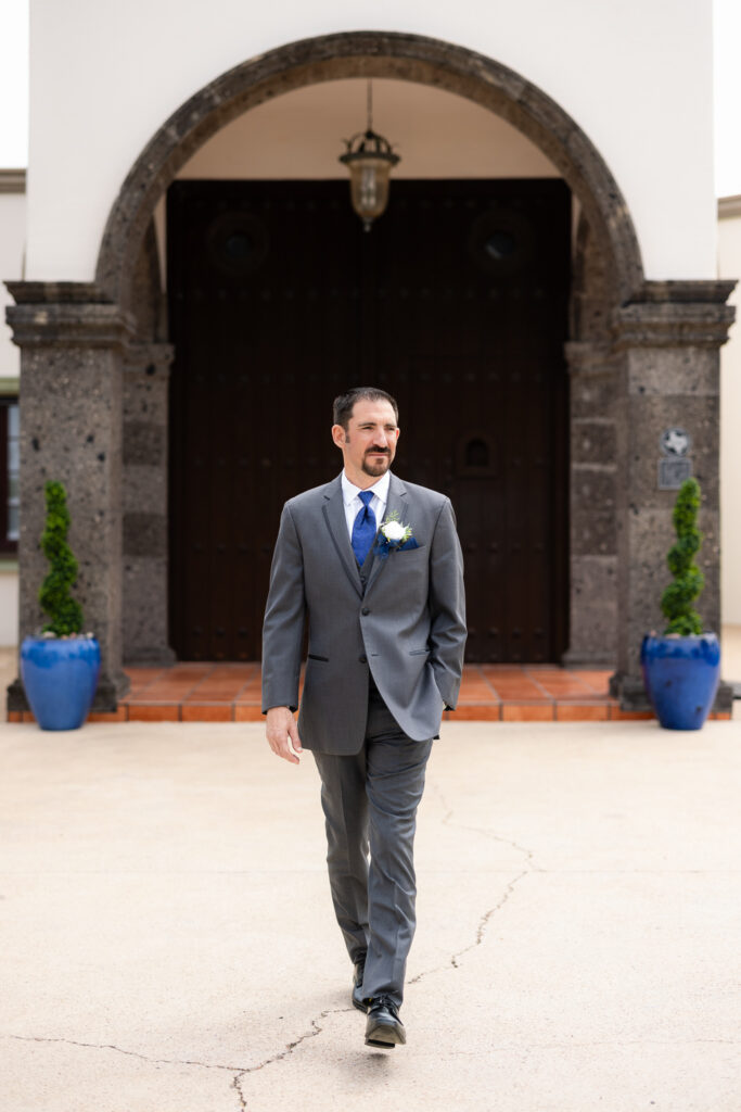 Groom walking with hand in pocket in front of Azle TX wedding venue Stoney Ridge Villa