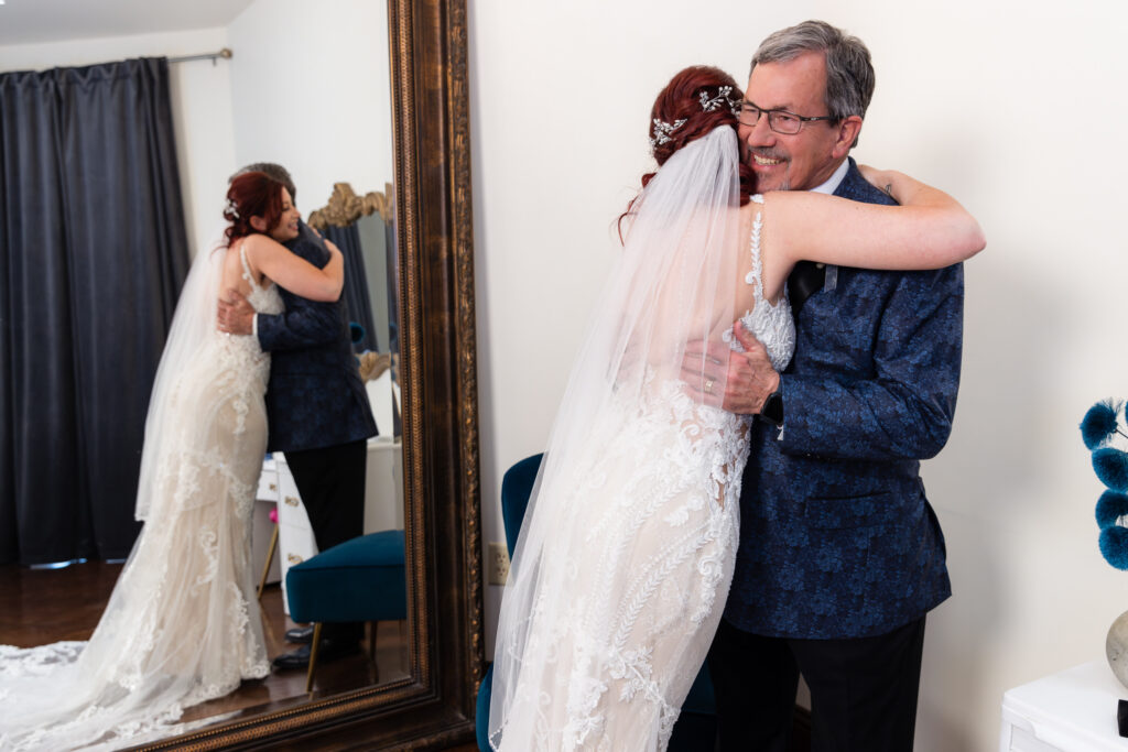 Bride hugging dad in front of large mirror in bridal suite