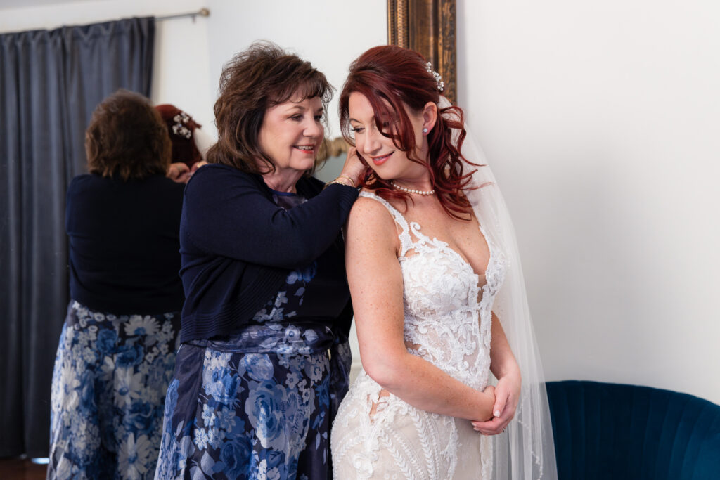 Mom putting pearl necklace on bride in front of large mirror in Stoney Ridge Villa bridal suite