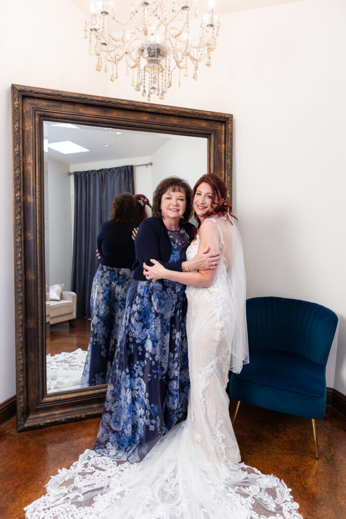 Bride hugging mom in front of large mirror in Stoney Ridge Villa bridal suite under crystal chandelier