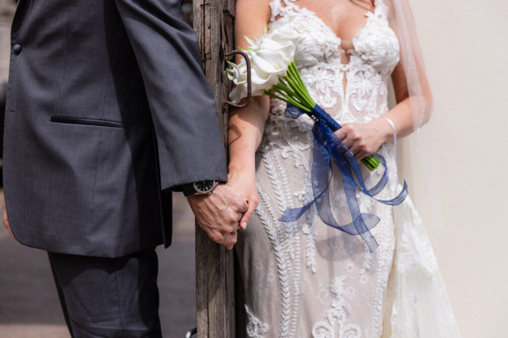 Bride and groom holding hands behind old wooden door for first touch while bride holds white tulip bouquet