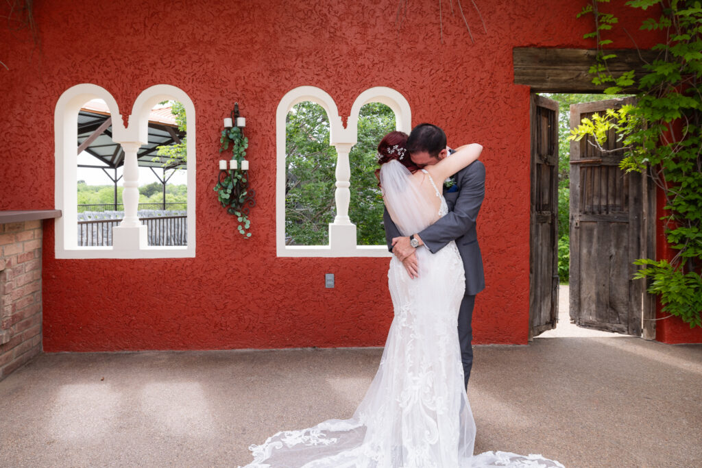 Groom crying and nuzzling into bride's neck after first look during wedding with orange wall as backdrop