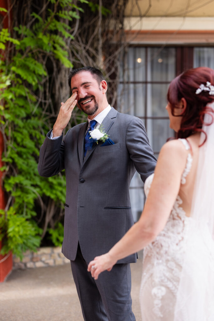 Groom crying and wiping tears during first look