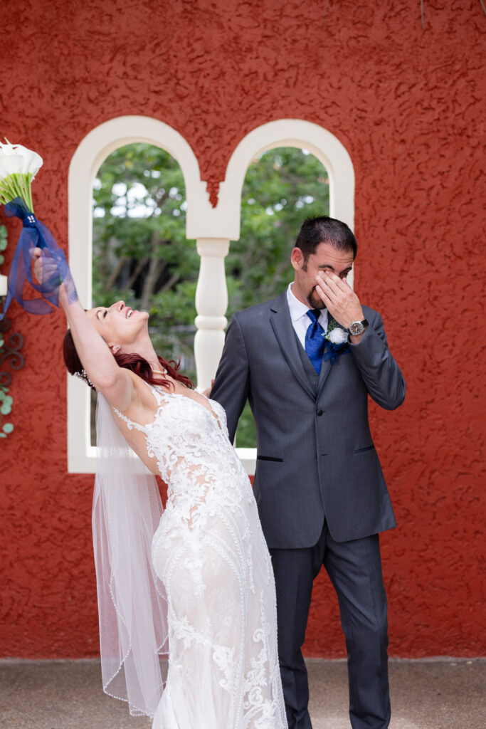 Bride cheering and throwing bouquet in air while groom wipes tears