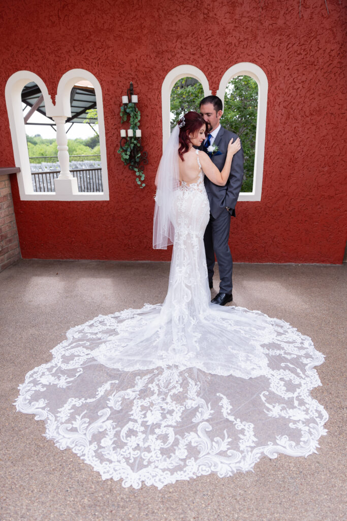 Bride and groom posing together in front of orange wedding venue wall with intricate and elegant wedding train sprawled out