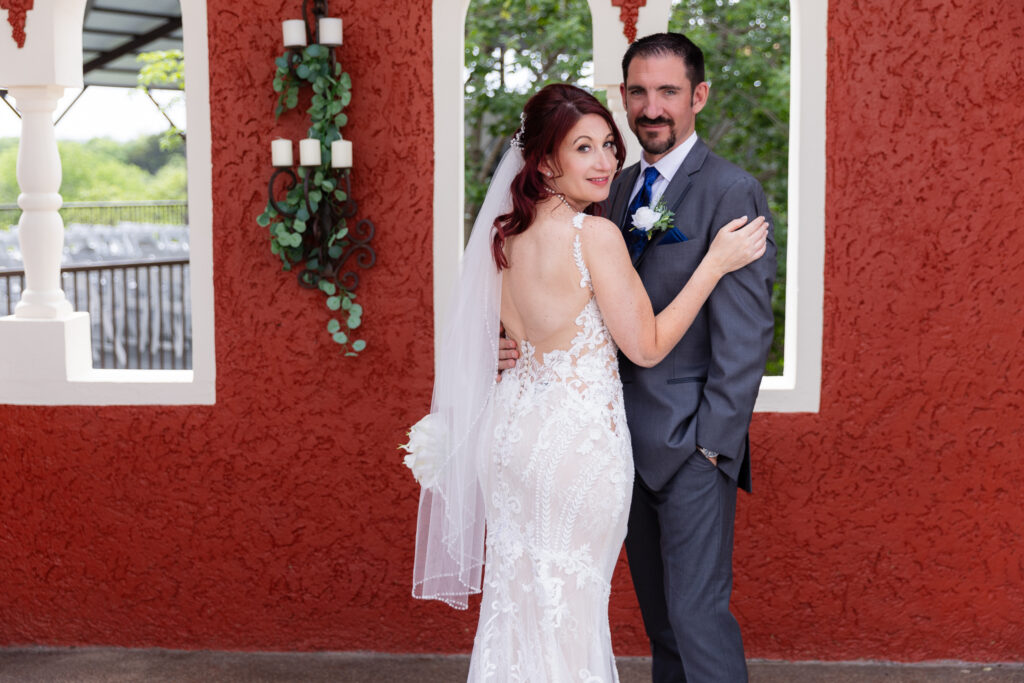 Bride looking back at camera while hugging groom in front of orange wedding venue wall