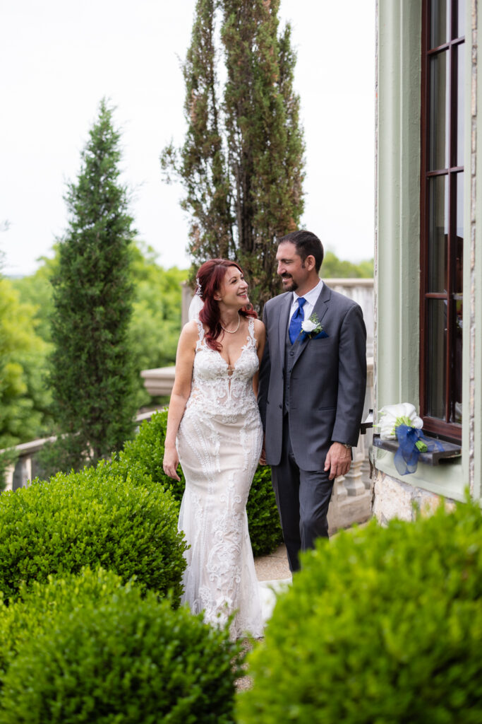 Bride and groom smiling at each other and walking surrounded by trees and bushes