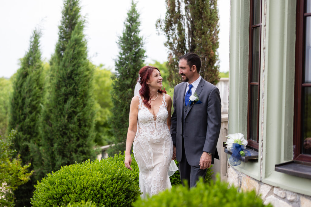 Bride and groom smiling at each other surrounded by trees and bushes