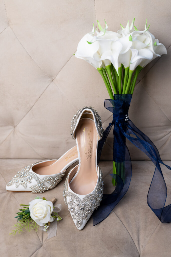 Bedazzled wedding shoes with white boutonniere and white tulip bouquet with blue ribbon