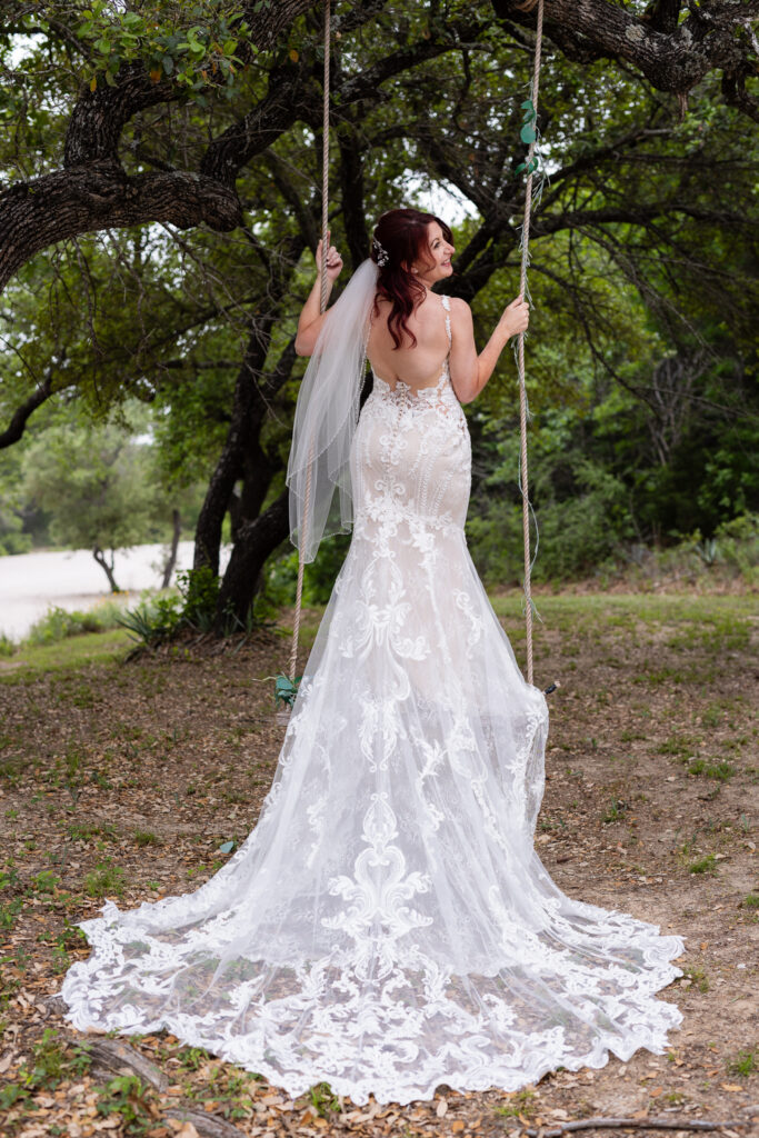 Bride on tree swing with intricate and elegant wedding dress train flowing down