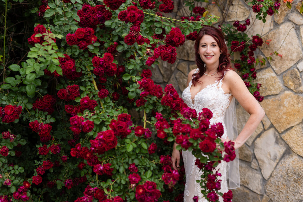 Red-haired bride smiling in wedding dress and veil surrounded by red roses