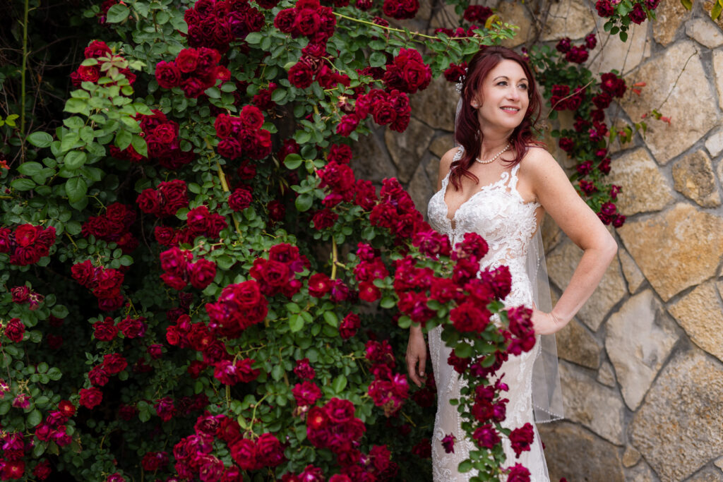 Red-haired bride looking off in wedding dress and veil surrounded by red roses