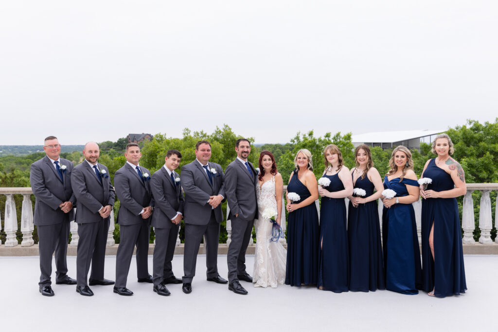 Wedding party in grey suits and blue dresses smiling in a line