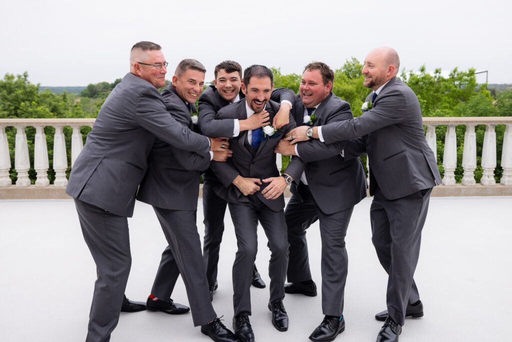 Groomsmen in grey suits jumping on groom laughing