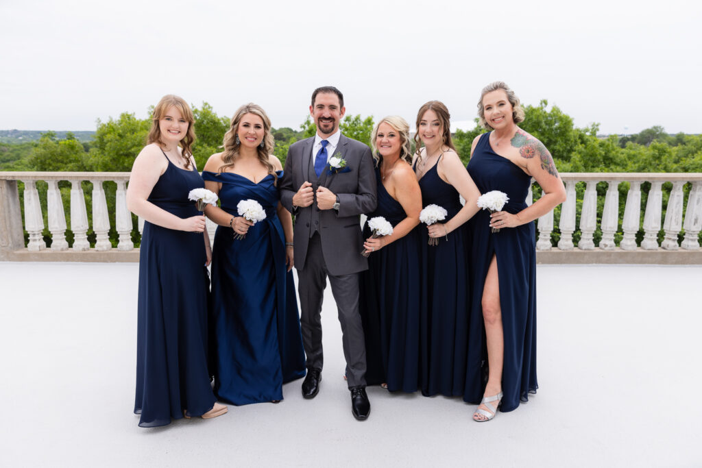 Groom in grey suit surrounded by bridesmaids in blue dresses smiling