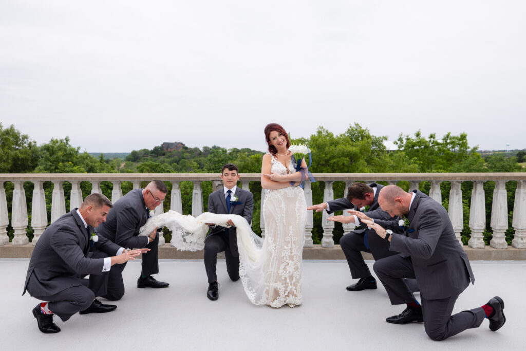 Bride with groomsmen in grey suits and blue ties bowing down to standing laughing bride