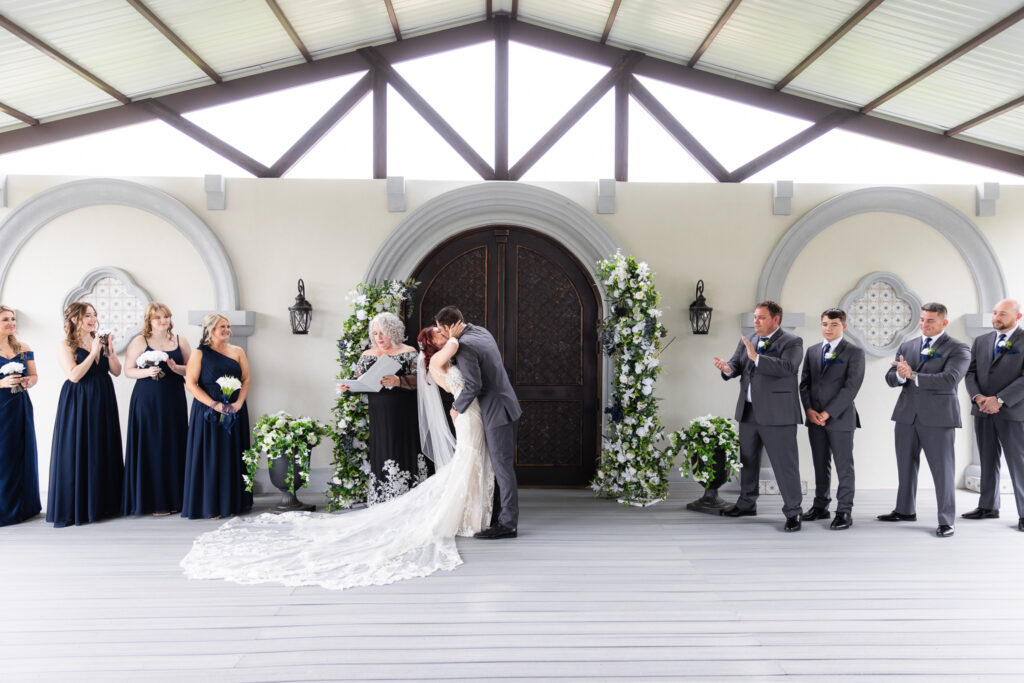 Bride and groom dip first kiss with wedding party clapping for them