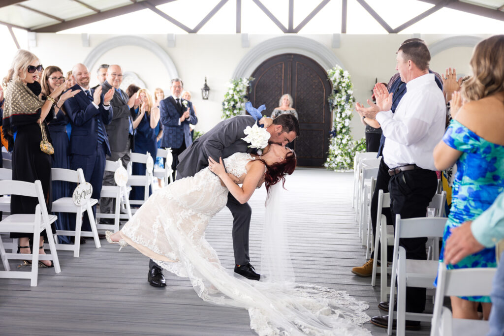 Bride and groom dip kiss down the aisle after ceremony with guests clapping and cheering