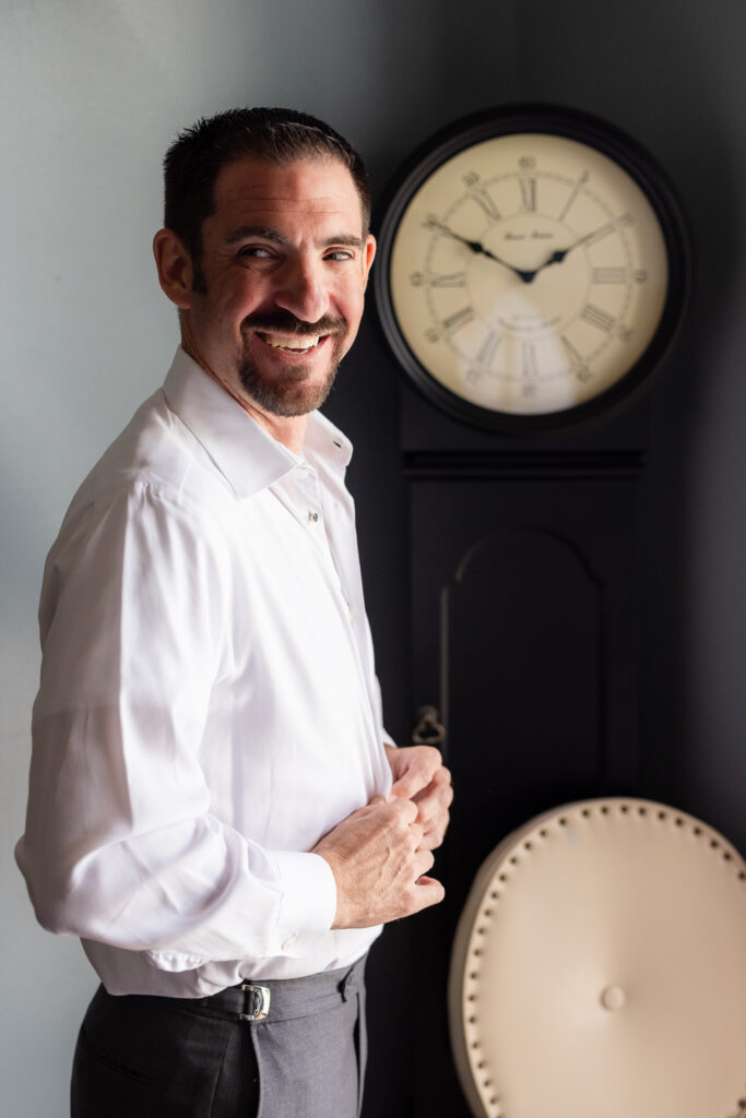 Groom buttoning up dress shirt with old clock in the background