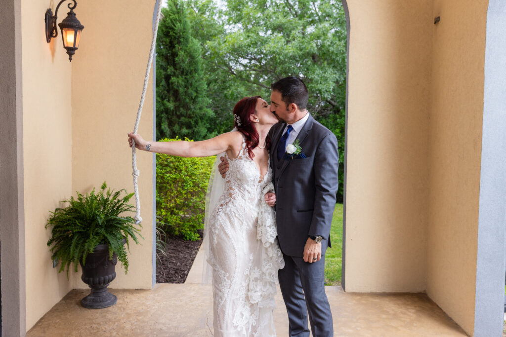 Bride and groom holding rope to bell tower while kissing at Azle TX wedding venue Stoney Ridge Villa