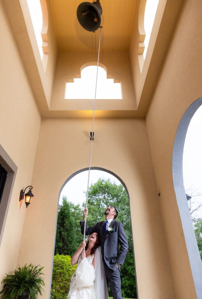 Bride and groom laughing while pulling the rope to bell tower at Azle TX wedding venue Stoney Ridge Villa