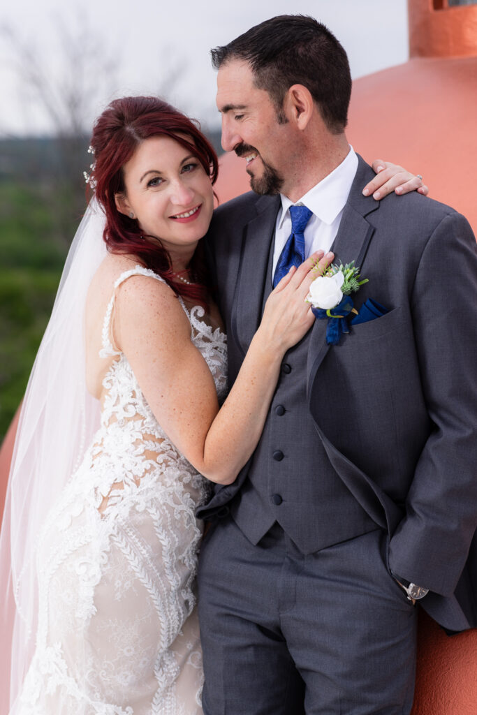 Red-haired bride smiling at camera while groom in grey suit laughs at her