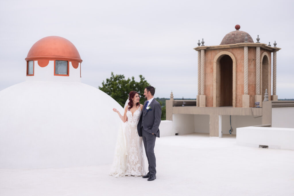 Bride and groom standing on wedding venue rooftop near bell tower