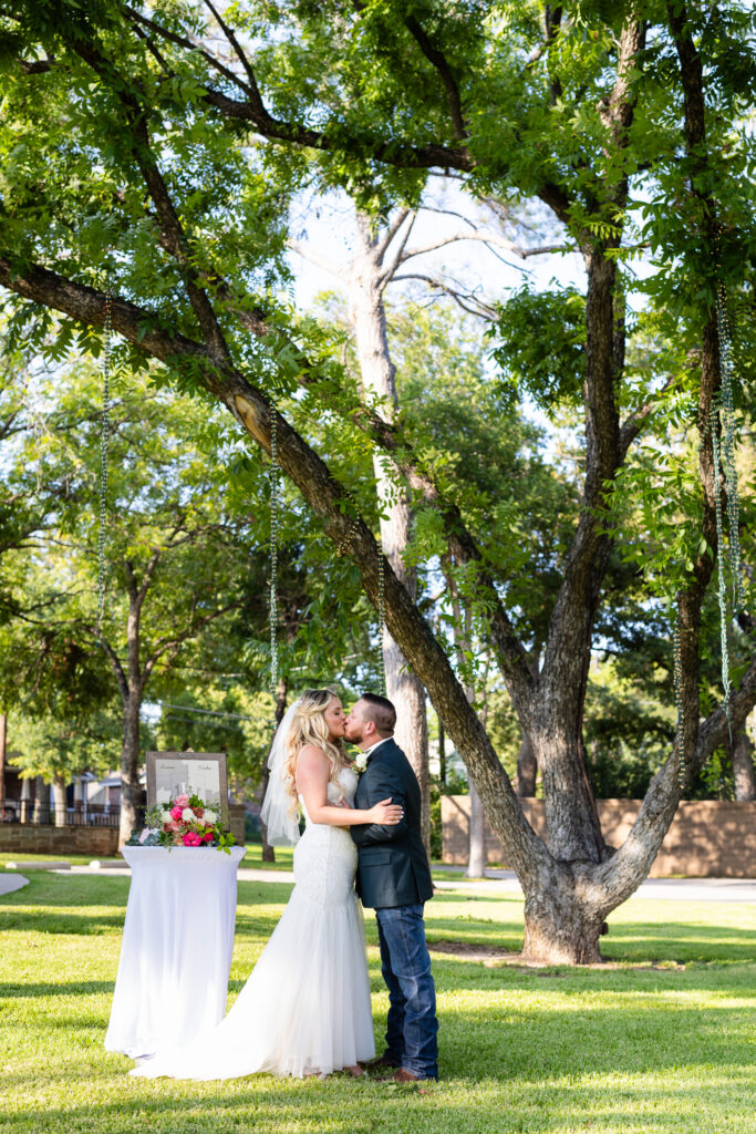 Bride and groom kissing for their First Kiss under big beautiful trees on Hotel Lucy lawn during intimate elopement ceremony