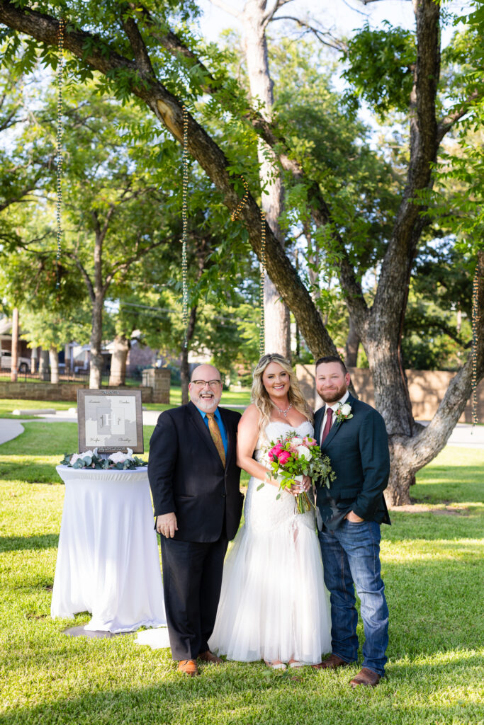 Bride, groom and officiant smiling at the camera after ceremony under big trees