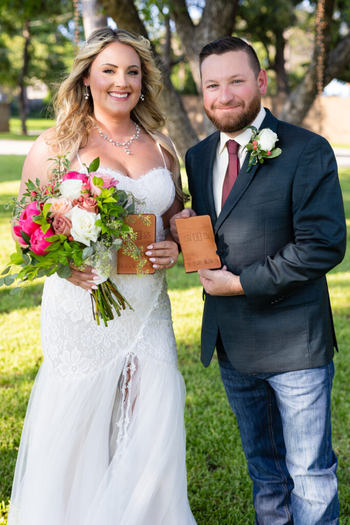 Bride and groom holding leather bound vow books and smiling at camera