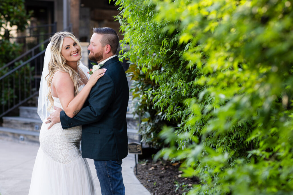 Bride and groom hugging next to hedge at Hotel Lucy in Granbury 