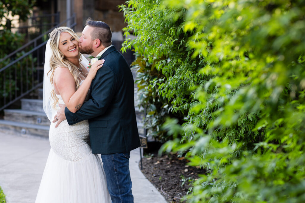 Groom kissing bride next to hedge