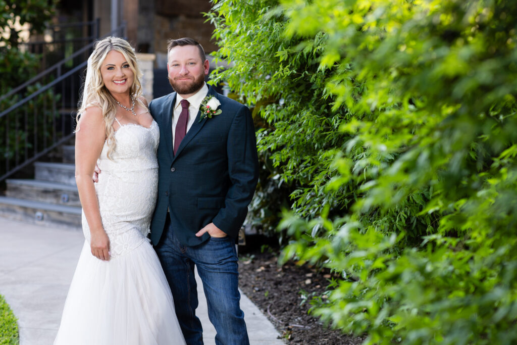 Bride and groom smiling next to hedge