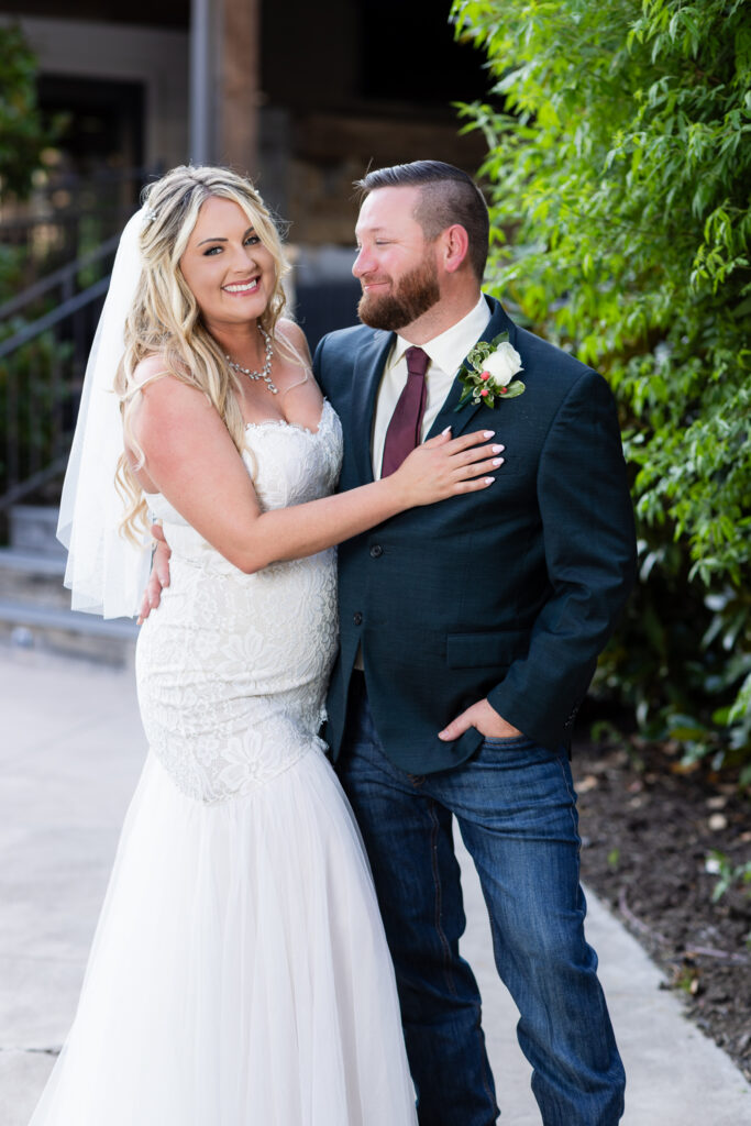 Bride and groom hugging and smiling next to hedge