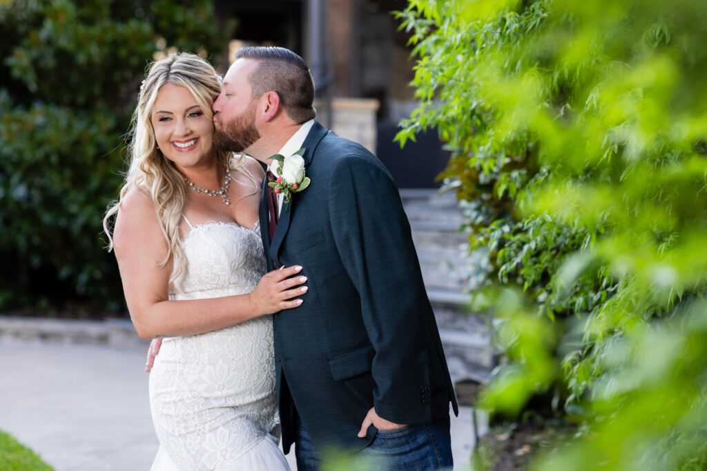 Groom kissing bride on temple while she smiles over her shoulder