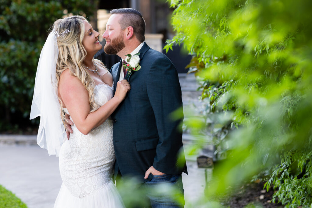 Bride and groom smiling into each other's eyes next to hedge on Hotel Lucy property during elopement