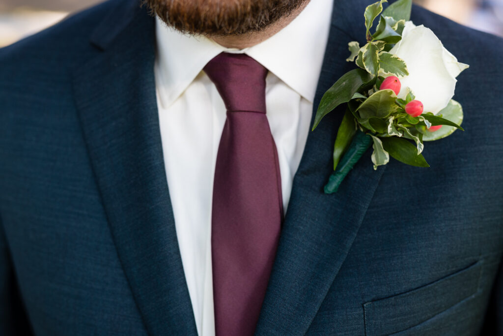 Close up of dark grey suit with burgundy tie and white and green boutonniere