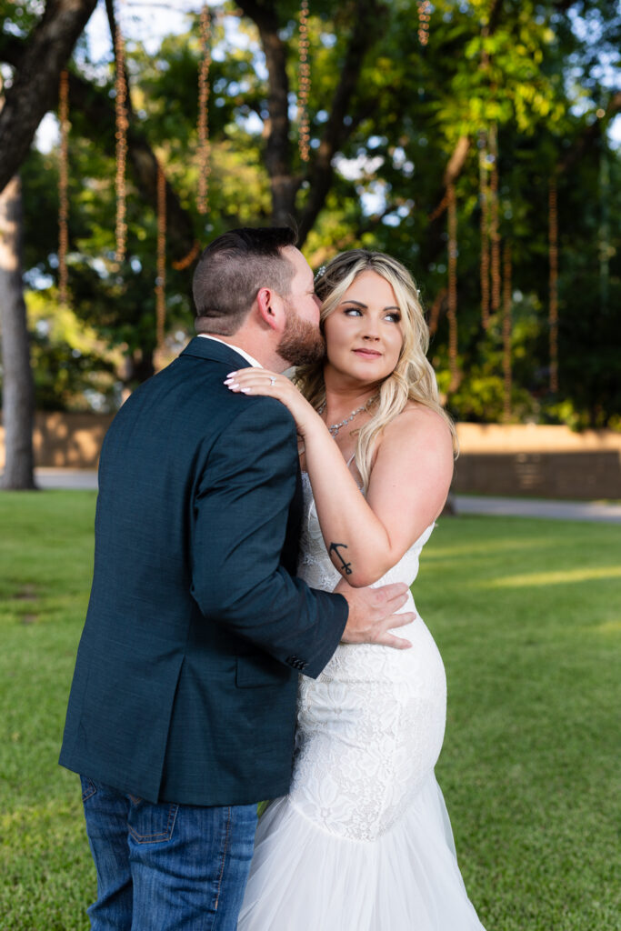 Groom kissing bride on temple under trees and hanging string lights