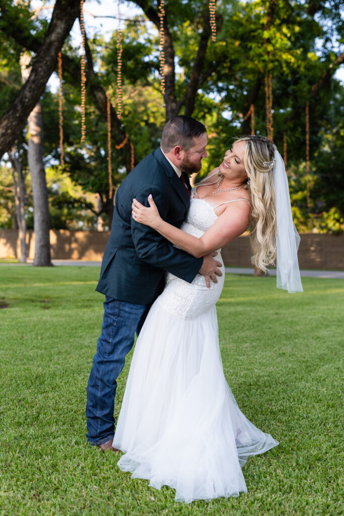 Groom dipping bride under trees and hanging string lights