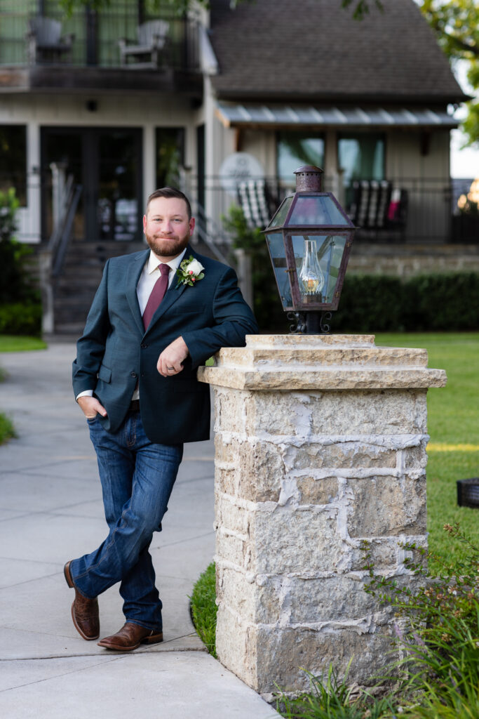 Groom leaning against light post with legs crossed