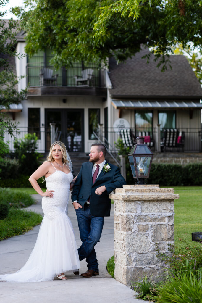 Groom leaning against light post with legs crossed and bride standing with hand on hip